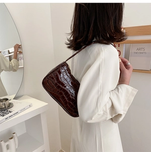 Detail of a dark brown crocodile pattern underarm bag shown with white dress styling