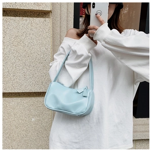 Close-up of a light blue minimalist baguette bag worn on shoulder with a white sweatshirt