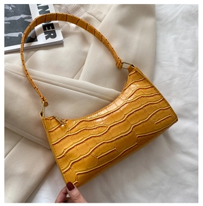 Primer plano del bolso de hombro amarillo con textura de cocodrilo sobre blazer beige