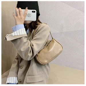 Detail of a beige minimalist baguette bag worn on shoulder over a khaki blazer