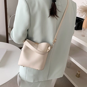 Minimalist cream white bucket bag with adjustable strap worn by model in suit