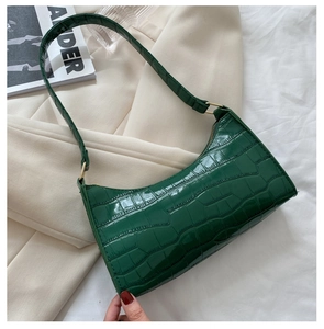 Detalle de bolso bajo el brazo verde oscuro con patrón de cocodrilo y cadena dorada