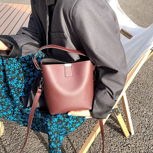 Minimalist burgundy leather bucket bag with top handle and shoulder strap shown in lifestyle use