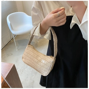 Close-up of beige baguette bag with crocodile embossed texture on a stylish model