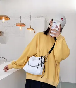 White bucket bag with butterfly print, silver chain, and wide black strap worn over yellow hoodie