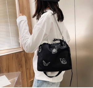 Detail of black drawstring bucket bag featuring silver butterfly prints and chain strap