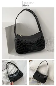 Detail view of black crocodile pattern faux leather baguette bag with golden metal zipper