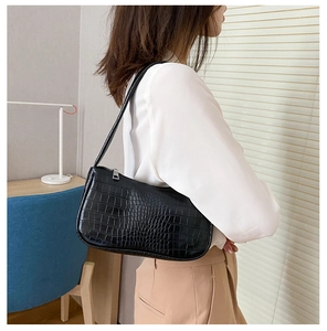 Détail du sac baguette noir motif crocodile porté à l'épaule par un mannequin en intérieur