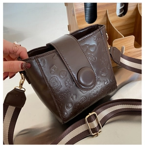 Detail of vintage brown bucket bag with embossed patterns and wide striped shoulder strap