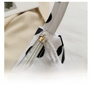 Detail of cow print tote bag featuring a gold zipper and woven rope pull handle
