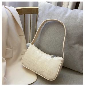 Détail d'un sac baguette crème avec texture crocodile posé sur un canapé gris
