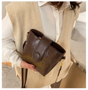 Detailed close-up of dark brown embossed leather bucket bag with wide striped strap