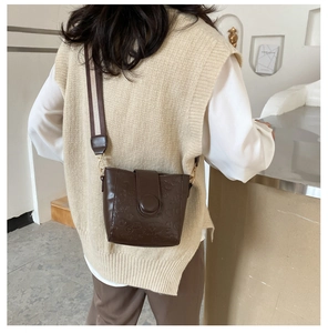 Detail of vintage brown leather bucket bag with cute animal embossing and wide woven strap