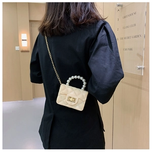 Detailed view of cream mini crossbody bag with pearl handle and metal chain strap on model