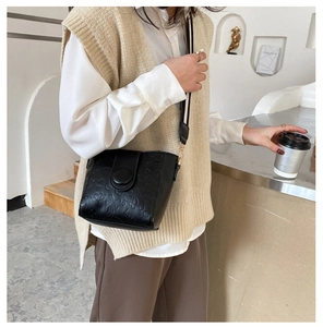 Detailed view of black bucket bag with embossed patterns and striped woven shoulder strap