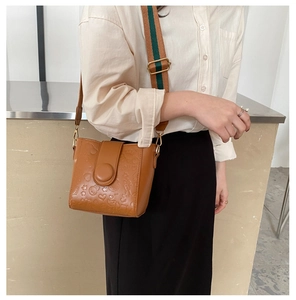 Brown bucket bag detail showing cartoon embossing and striped wide canvas strap