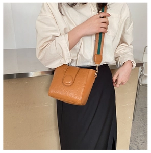 Detail of a brown bucket bag featuring cartoon embossed patterns and a wide fabric strap