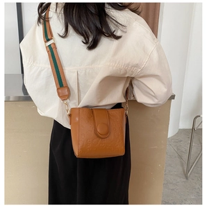 Detail of a brown bucket bag featuring embossed patterns and a wide striped strap