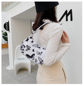 Detail shot of white canvas shoulder bag featuring black butterfly prints and sleek strap