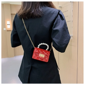 Close-up of a red quilted jelly bag with pearl handle and gold chain strap on model