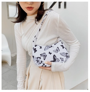 Side view of a white shoulder bag featuring black butterfly patterns on a female model