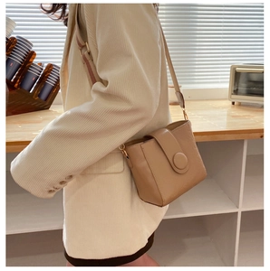Detail of beige embossed faux leather crossbody bucket bag with wide strap on a model
