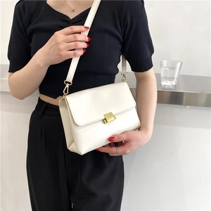 Minimalist white leather crossbody bag with golden buckle held by a model in black outfit