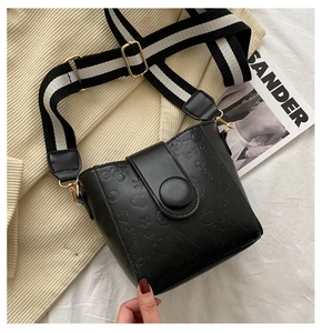 Detail of black leather bucket bag with embossed patterns and striped wide shoulder strap