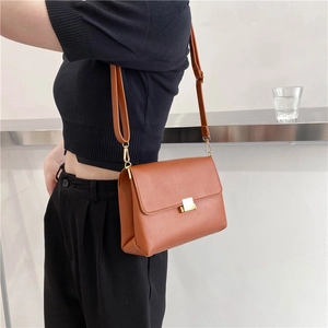 Minimalist brown leather crossbody bag with golden metal clasp shown on female model