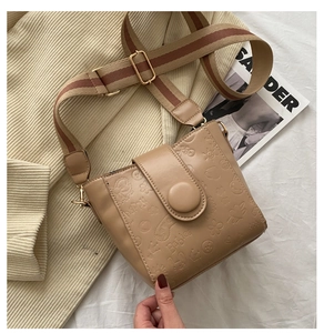 Close-up of khaki embossed bucket bag with wide striped strap on a minimalist background