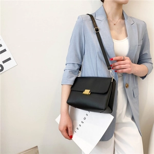 Minimalist black faux leather shoulder bag with gold square metal buckle on a stylish model