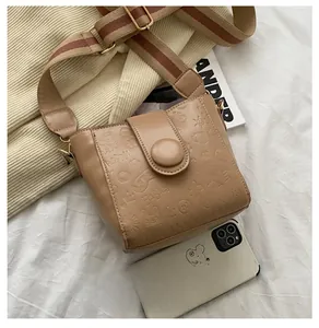 Detailed shot of khaki crossbody bag with cartoon embossing and wide striped strap