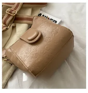 Detail showing retro khaki bucket bag with cartoon embossing and wide striped strap