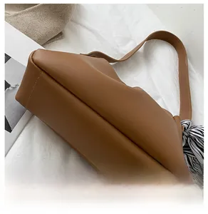 Detailed view of brown leather bag base with stitching and decorative striped scarf