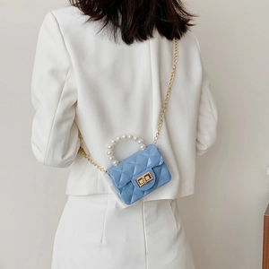 Mini light blue quilted chain handbag with pearl handle and golden twist lock on white blazer