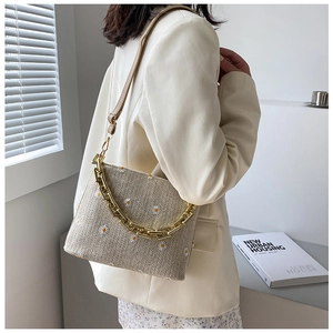 Detail der beigen gewebten Tasche mit Gänseblümchenstickerei und goldener Kette