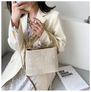Detail der beige gewebten Strohtasche mit weißer Margeritenstickerei und Goldkette