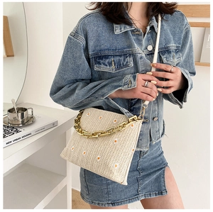 Nahaufnahme der gewebten Strohtasche mit Gänseblümchen, Goldkette und weißem Riemen