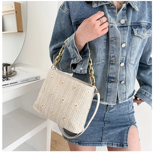 Detail einer beigen geflochtenen Strohtasche mit Gänseblümchen-Stickerei und Goldkette