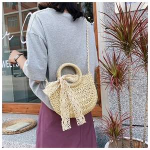 Detail of handwoven straw bag with a cream lace bow shown in a lifestyle street setting