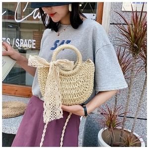 Outdoor shot of a woven half-moon straw bag with elegant cream lace bow detail