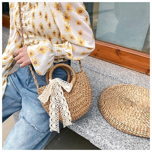 Detail of handmade straw crossbody bag with white lace bow and dual handles