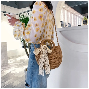 Detail of hand-woven straw crossbody bag with lace bow and dual handles on a model