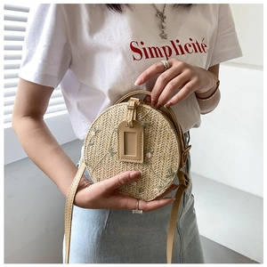 Detail of round straw crossbody bag featuring floral embroidery and a leather shoulder strap
