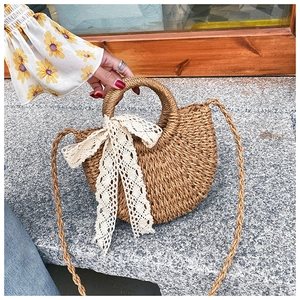 Close-up of a woven straw bag with lace bow, round handle and shoulder strap