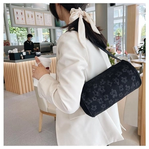 Detail of black cylindrical shoulder bag with 3D floral texture and fabric strap