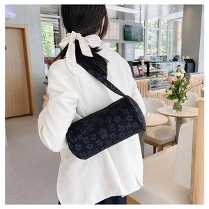 Detail of a black cylindrical shoulder bag with floral embossing worn over a white blazer