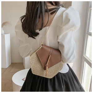 Detail view of woven straw and brown leather bag with tassel and gold chain