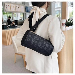 Detail of a black cylindrical shoulder bag with 3D floral patterns worn by a person