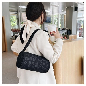 Detail view of black barrel bag with textured floral fabric worn over the shoulder